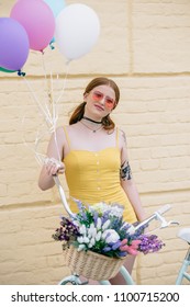 beautiful young woman in sunglasses smiling at camera while standing with bicycle and colorful balloons on street