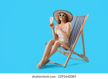 Hermosa joven con crema de protección solar sentada en la tumbona sobre fondo azul