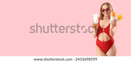 Beautiful young woman in swimsuit holding sunscreen creams on pink background with space for text