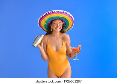 Beautiful young woman in swimsuit, sombrero hat and with cocktail against color background