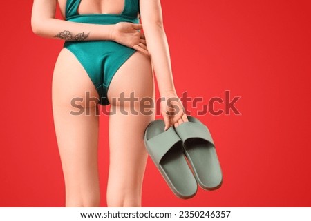 Beautiful young woman in swimsuit with stylish flip flops on red background, back view