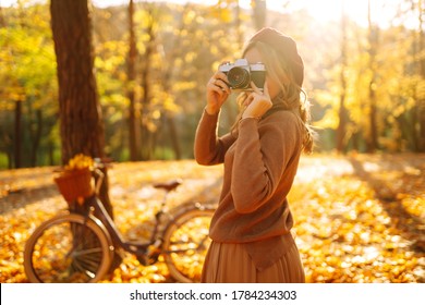 Beautiful young woman takes photos with a retro camera in autumn forest. Smiling girl enjoying autumn weather. Rest, relaxation, lifestyle concept. - Powered by Shutterstock