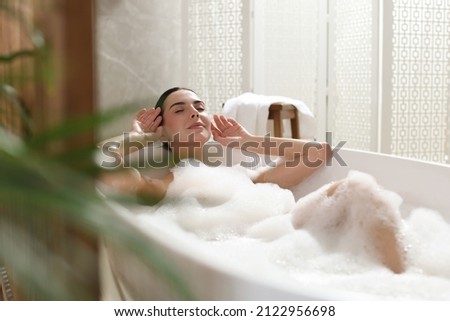Beautiful young woman taking bubble bath at home