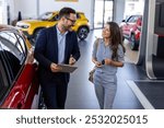 Beautiful young woman is talking to handsome car dealership worker while choosing a car in dealership