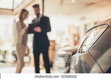 Beautiful Young Woman Is Talking To Handsome Bearded Sales Manager While Choosing A Car In Dealership