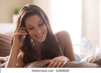 Beautiful Young Woman Talking On The Phone While In Bed 