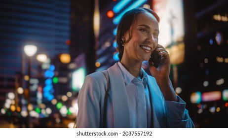 Beautiful Young Woman Talking on Smartphone Walking Through Night City Street Full of Neon Light. Portrait of Gorgeous Smiling Female Answering Mobile Phone in Stylish Urban Area. - Powered by Shutterstock