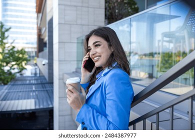 Beautiful young woman talking on her mobile phone and smiling at the staircase drinking coffee. Beautiful business woman having take away cafe and working on her phone - Powered by Shutterstock