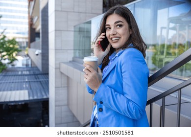 Beautiful young woman talking on her mobile phone and smiling at the staircase drinking coffee. Beautiful business woman having take away cafe and working on her phone - Powered by Shutterstock