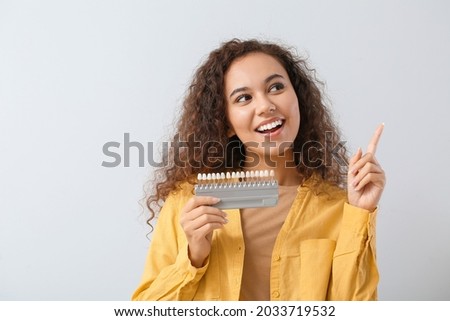 Beautiful young woman with teeth samples showing something on light background