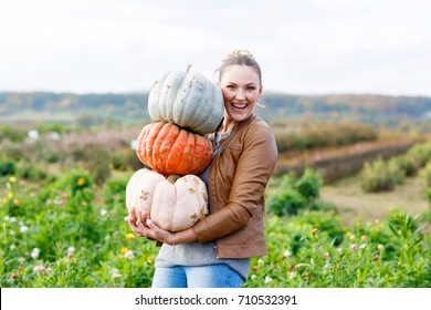 Beautiful young woman with three huge different pumpkins on a farm or patch. Girl having fun with farming. Thanksgiving or halloween. Harvesting time on autumn