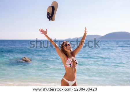 Beautiful young woman throwing hat in the air at the beach while smiling