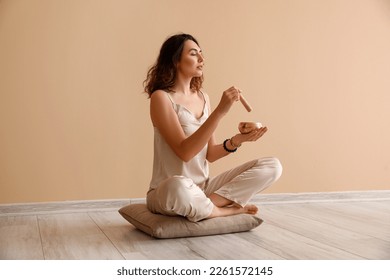 Beautiful young woman with Tibetan singing bowl sitting near beige wall