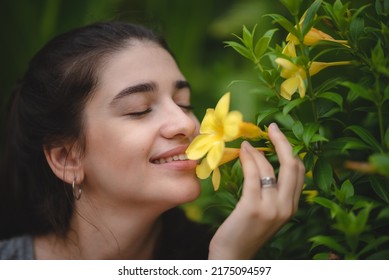 Beautiful young woman with toothy smile feeling and smelling beautiful yellow flower while in nature enjoying and relaxing with closed eyes - Shutterstock ID 2175094597