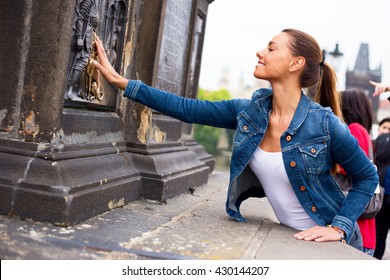 a beautiful young woman touching the bronze plaque on charles bridge for good luck