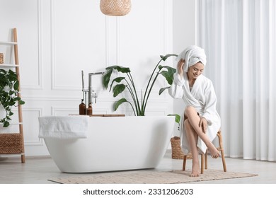 Beautiful young woman touching her smooth legs in bathroom, space for text - Powered by Shutterstock