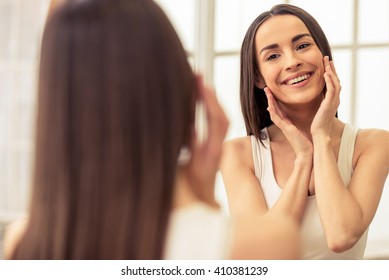 Beautiful Young Woman Is Touching Her Face And Smiling While Looking At The Mirror