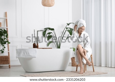 Beautiful young woman touching her smooth legs in bathroom, space for text
