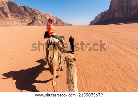 beautiful young woman tourist in white dress riding on camel in wadi rum desert, Jordan