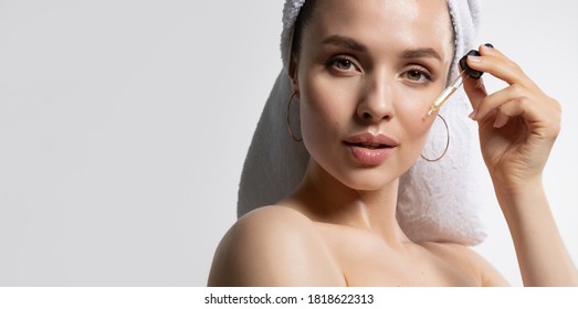 Beautiful young woman in towel apply moisturizing facial serum isolated on white background. Morning daily beauty luxury procedures. Skincare and rejuvenation concept