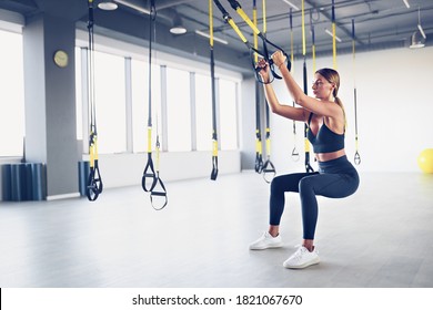 Beautiful young woman training with suspension trainer sling or suspension straps in gym. Upper body exercise concept on TRX.