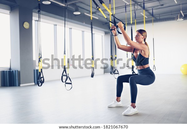 Beautiful young woman training with suspension\
trainer sling or suspension straps in gym. Upper body exercise\
concept on TRX.