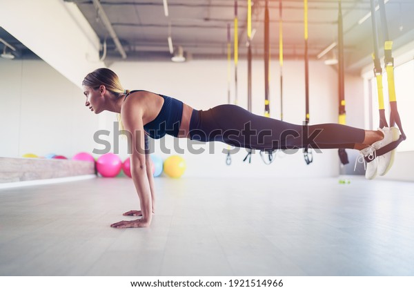 Beautiful young woman training with\
suspension trainer sling or suspension straps in\
gym.
