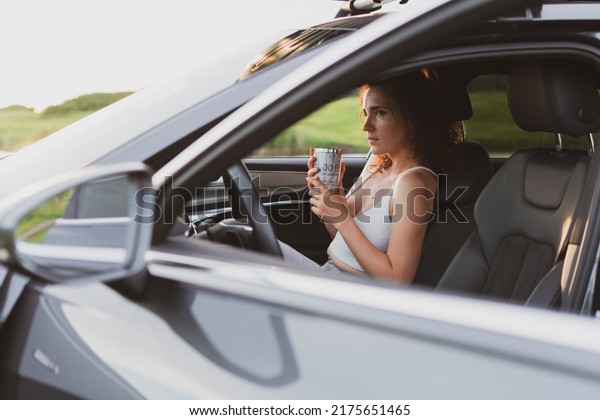 beautiful young woman travel on the roads by car,\
stopped at the side of the road and look at the map, drink coffee\
from a thermos. Vacation\
concept