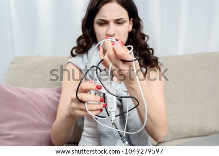 Beautiful young woman tries to untangle tangled wire and headphones. Female hands holds tangled wires from smartphone