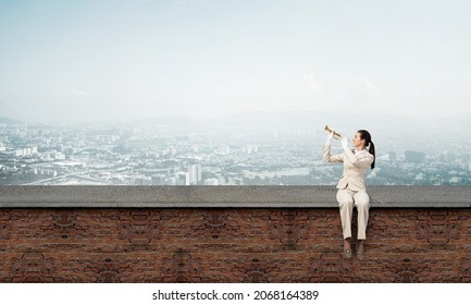 Schöne junge Frau mit Trompete auf dem Dach. Braves Mädchen in weißem Business-Anzug mit Musik-Messing-Instrument auf dem Dach sitzend. Mixed Media Business Concept. Musikerin