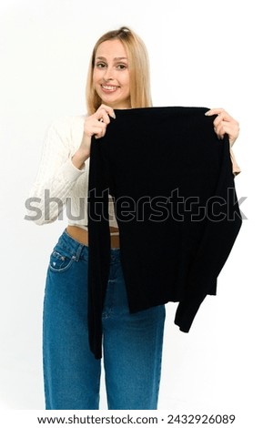 Beautiful young woman trying on a black sweater. Trying on clothes. Blonde girl with a black jumper on a white background.