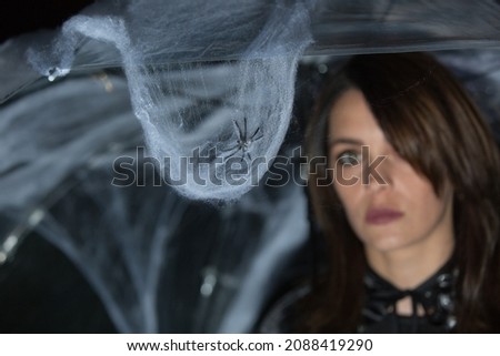 Beautiful young woman under an umbrella with cobwebs and spiders on a Halloween picnic. Focus on the spider. Warm autumn October evening. Magic mood. Emotion concept.