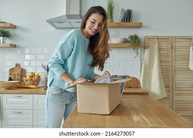 Beautiful Young Woman Unpacking Box While Standing At The Domestic Kitchen