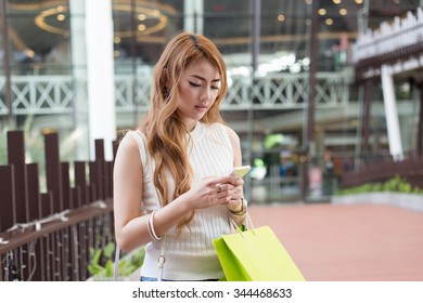 Beautiful Young Woman Use Mobile Phone And Holding Shopping Bag