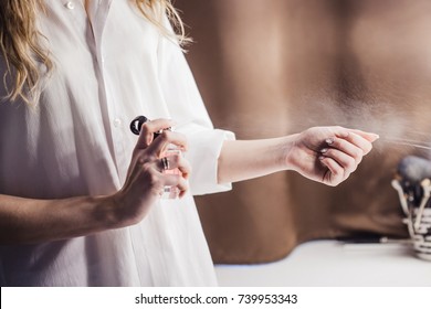 Beautiful young woman uses bottle of perfume at home, closeup