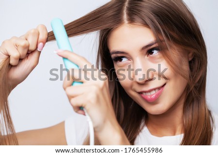 Beautiful young woman uses a hair straightener to make a beautiful styling