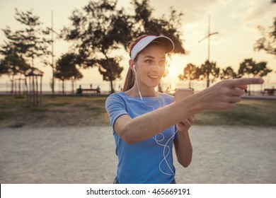 Beautiful young woman is using an app in her smartphone device to play a gps based augmented reality mobile game in the park, pointing to a direction of a possible reward