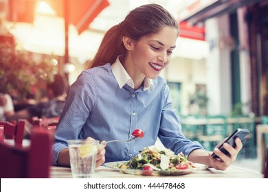 beautiful young woman using an application to send an sms message in her smartphone device while eating a salad - Powered by Shutterstock