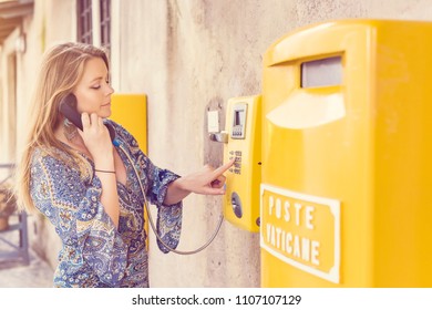 Beautiful Young Woman Using A Coin Operated Public Payphone On The Street