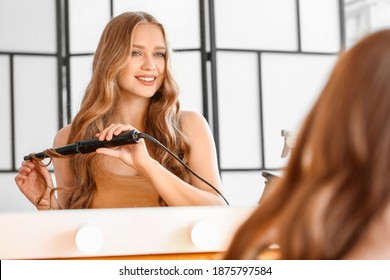 Beautiful young woman using curling iron for hair at home