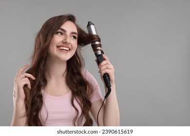 Beautiful young woman using curling hair iron on grey background, space for text - Powered by Shutterstock