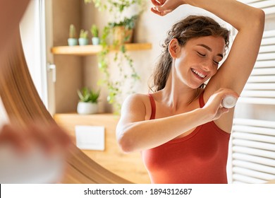 Beautiful young woman using deodorant under armpit in bathroom during morning time. Girl applying deodorant roll on after shower on underarms. Girl using antiperspirant roll-on at home after waking up