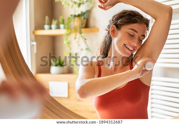 Beautiful young woman using deodorant under armpit in\
bathroom during morning time. Girl applying deodorant roll on after\
shower on underarms. Girl using antiperspirant roll-on at home\
after waking up