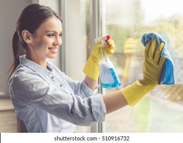 Beautiful Young Woman Is Using A Duster And A Spray And Smiling While Cleaning Windows In The House