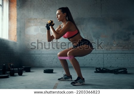 Beautiful young woman using elastic resistance band while exercising in gym