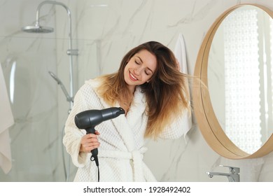 Beautiful young woman using hair dryer near mirror at home