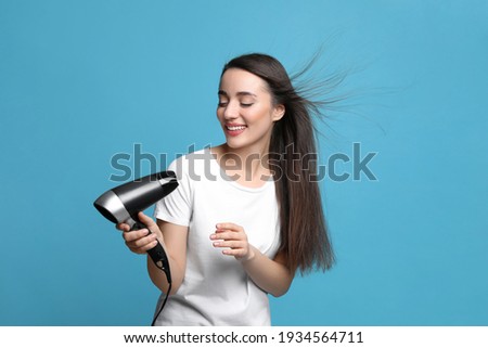 Beautiful young woman using hair dryer on light blue background
