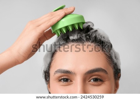 Beautiful young woman using hair scalp massager on grey background, closeup