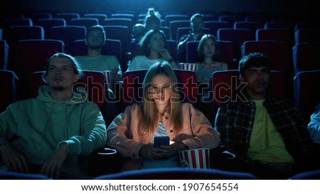 Beautiful young woman using her phone for texting while watching a movie at the cinema. Technology, entertainment concept. Front view. Web Banner