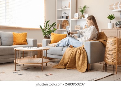 Beautiful young woman using laptop and relaxing on sofa in living room - Powered by Shutterstock